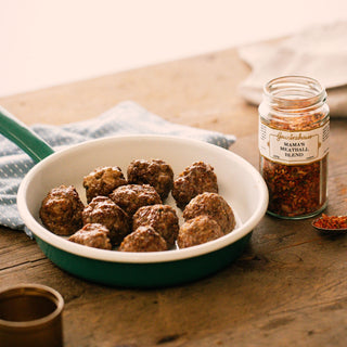 White pan with meatballs on a wooden table next to a jar of seasoning.