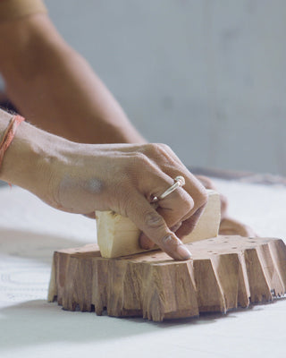 Person cutting a block of cheese on a wooden board with a blurred background