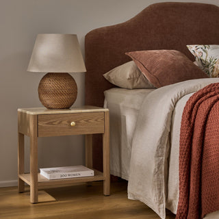 Bedroom scene with a wooden nightstand, lamp, and bed with pillows and blanket.