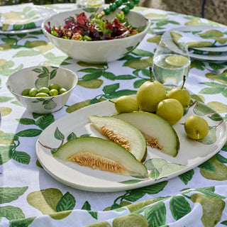 Table setting with melon, apples, and salad on a leaf-patterned tablecloth.