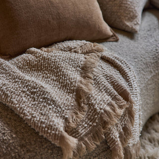 Close-up of a textured beige blanket with fringes on a soft surface.