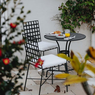 Outdoor patio set with black metal chairs and table, surrounded by plants and flowers.
