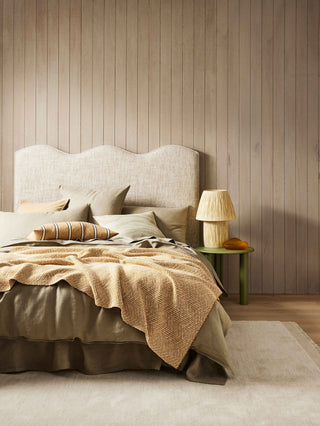Bedroom with wooden wall paneling, bed with beige bedding, cushion, and side table with lamp.