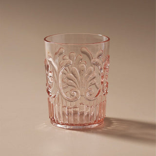 Decorative pink glass tumbler with embossed patterns on a beige background