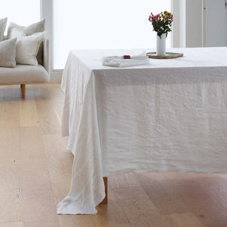 White tablecloth on a dining table with a vase of flowers in a minimalistic room.