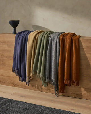 Set of five scarves in blue, beige, green, gray, and brown draped over a wooden surface.