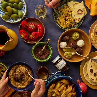Diverse array of food on a table with various dishes including flatbreads, vegetables, and dips.