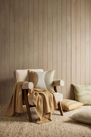 Cozy armchair with a blanket and pillows against a wooden paneled wall.
