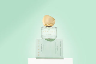 Perfume bottle with gold cap and matching box on a light green background