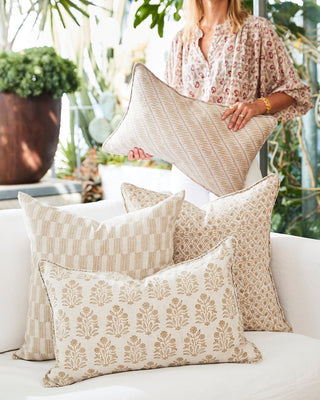 Person arranging decorative pillows on a white couch with a garden background
