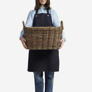 Person holding a large wicker basket wearing a black apron on a white background