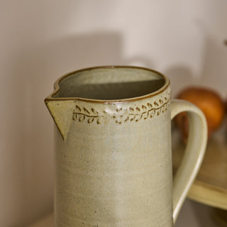 Ceramic pitcher with decorative lid on a neutral background