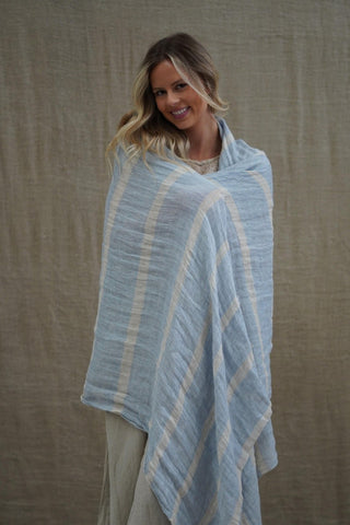 Woman wearing a light blue and white striped shawl against a beige background