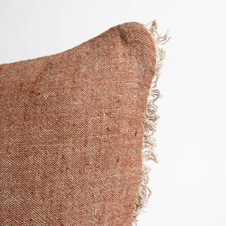 Textured brown pillow with frayed edge on a light gray background