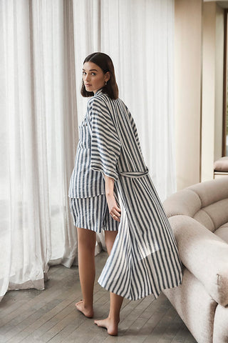 Woman wearing a black and white striped outfit standing in a room with curtains and a sofa.