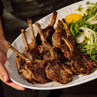 Plated rack of lamb with a side salad on a white plate.