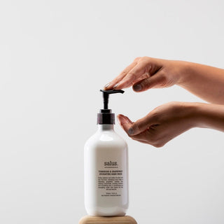 Person using a white hand soap bottle with pump on a light gray background