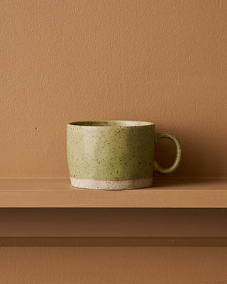 Green ceramic mug on a brown surface with a matching brown wall background
