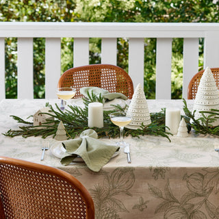 Decorated outdoor table with Christmas trees, candles, and greenery on a white railing background.