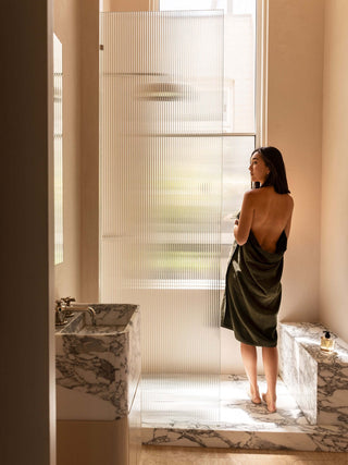 Woman in a green dress standing in a modern bathroom with marble fixtures.