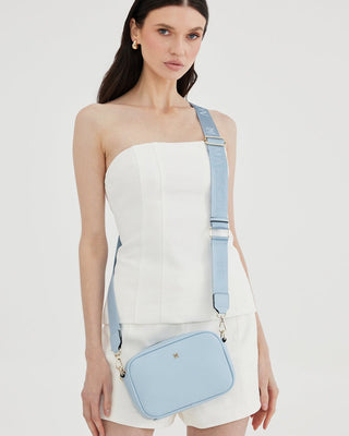 Woman wearing a strapless white top and light blue suspenders with a matching bag on a white background