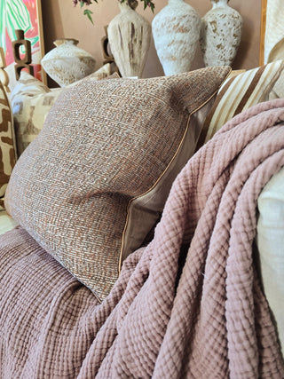 Textured pillow and pink blanket on a couch with decorative vases in the background