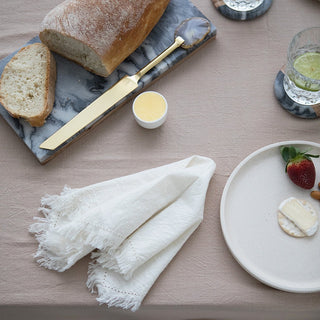 Loaf of bread with a knife, butter, napkin, and a plate with a strawberry and bread on a marble surface.
