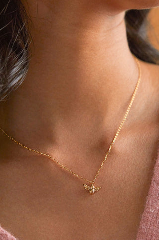 Gold necklace with a bee pendant on a person's neck