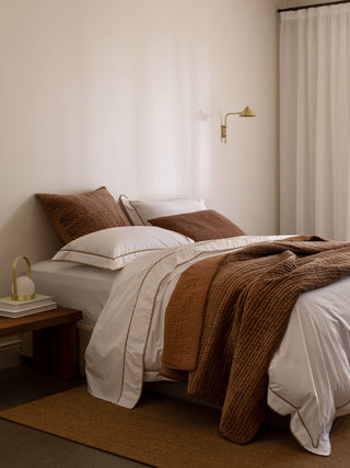 Neatly made bed with brown and white bedding in a bedroom setting.