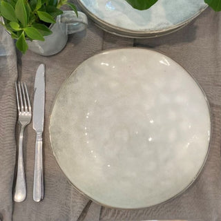 White ceramic plate with silver fork and knife on a gray surface, with a plant in the background.