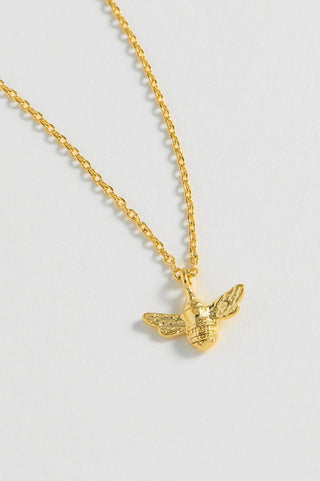 Gold bee pendant necklace on a light gray background