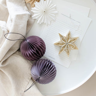 Decorative purple paper balls and a gold star on a white surface with beige fabric.