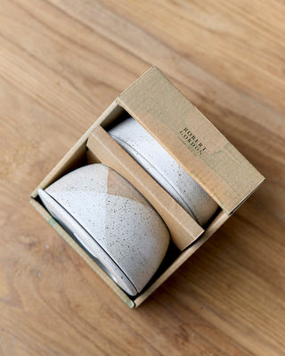 Two ceramic cups in a cardboard box on a wooden surface
