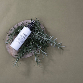 Skincare bottle on a wooden plate with green leaves against a beige background