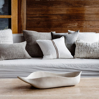 Gray sofa with decorative pillows and a white ceramic bowl on a wooden surface.
