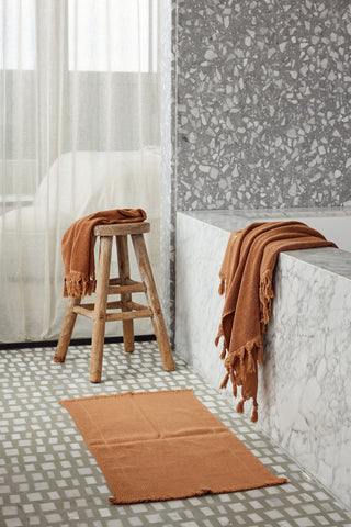 Bathroom with terrazzo tiles, a bathtub, and a stool with a towel.