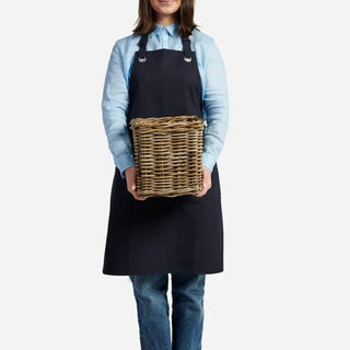 Person wearing a black apron holding a wicker basket on a white background