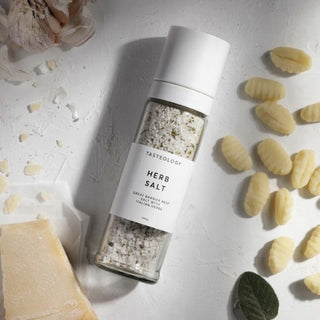Tastelology herb salt shaker on a light surface with gnocchi and herbs.