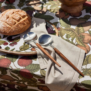 Two silver spoons with wooden handles on a floral tablecloth with bread and a bowl.