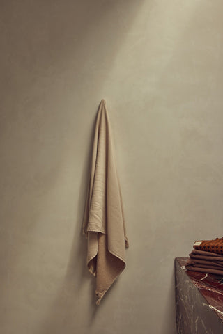 Beige towel hanging on a light green wall next to a wooden shelf.