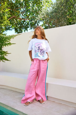 Person wearing a white t-shirt with a graphic design and pink pants with side stripes, standing outdoors.
