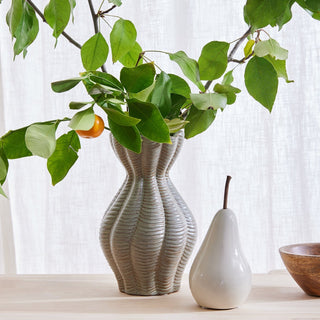 Decorative vases with a plant and fruit on a light surface with a white curtain background