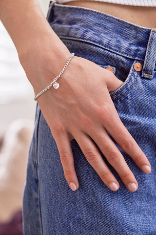 Hand wearing a silver bracelet with heart charms on a blurred denim background