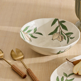 Ceramic bowl with pear design on a beige surface with utensils and another plate.