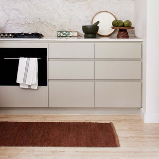 Modern kitchen with light gray cabinets, marble backsplash, and a red rug on the floor.