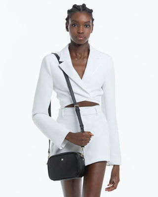Woman wearing a white suit holding a black handbag on a white background