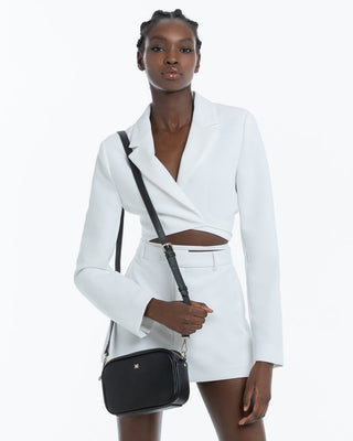 Woman wearing a white blazer with a black handbag on a white background