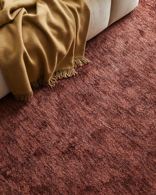 Close-up of a textured red carpet with a beige blanket draped over a corner.