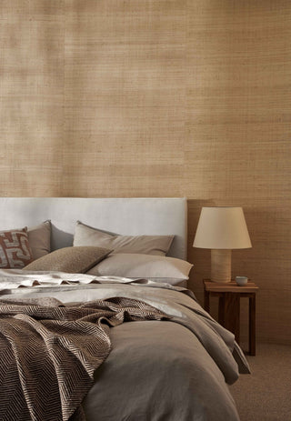 Bedroom with textured brown wallpaper, cushion, bed with patterned bedding, and lamp on nightstand.