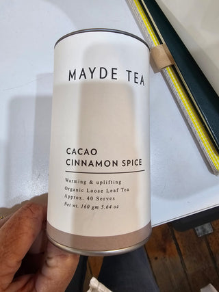 Mayde Tea Cacao Cinnamon Spice canister held by a hand with a blurred background